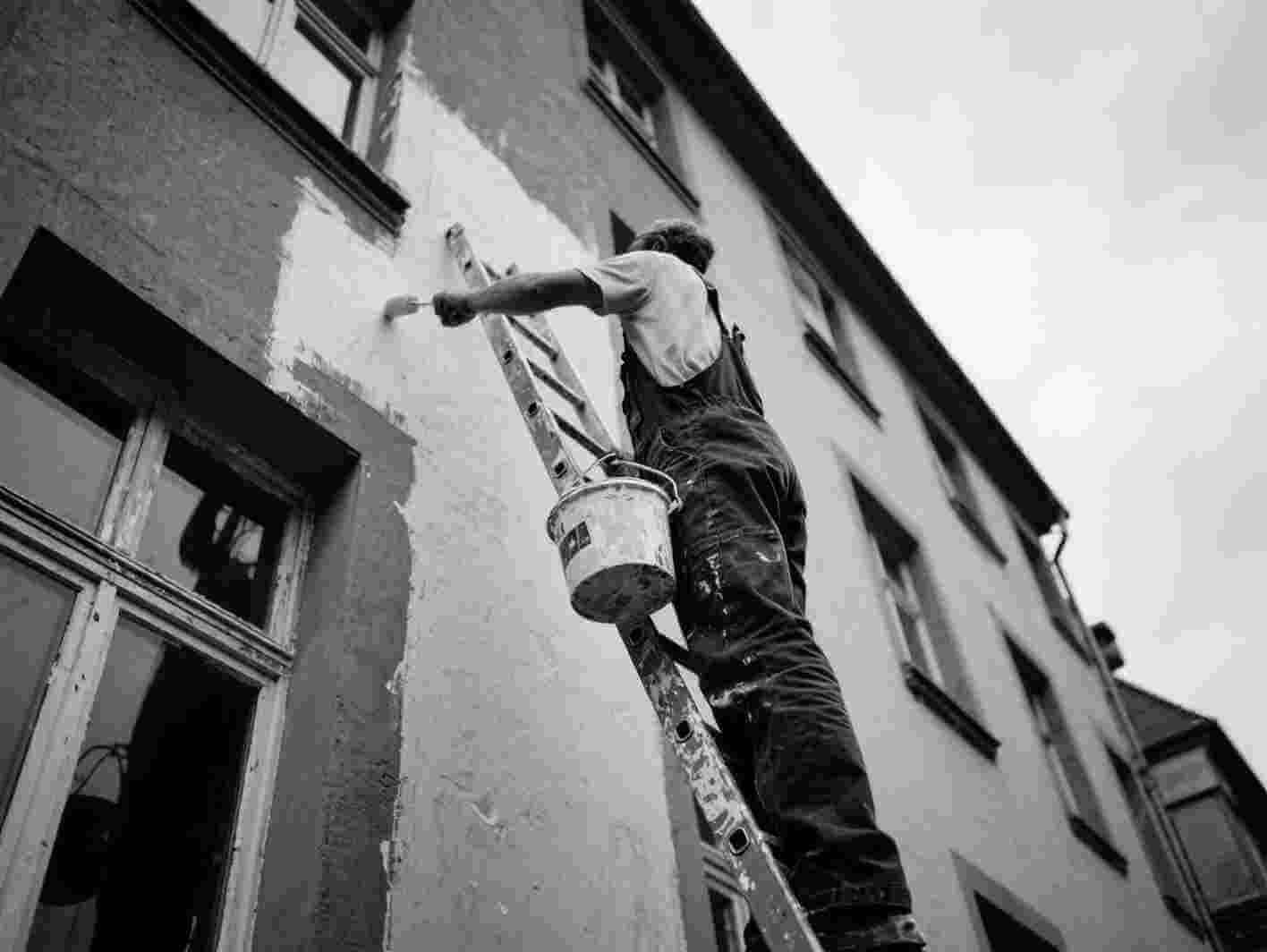 Maler auf einer Leiter beim Streichen der Fassade.
